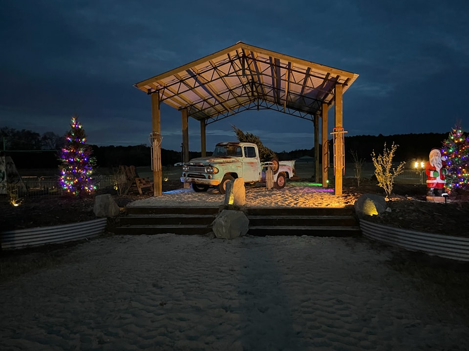 Vintage truck under the lit pavilion at dusk with Christmas trees and Santa decor for the holiday season