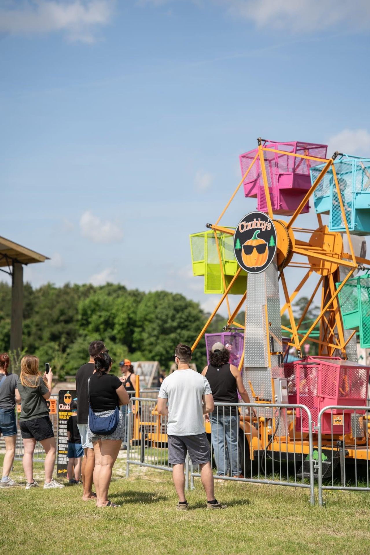 Families lined up watching the colorful Chubby's Ferris Wheel spin on a sunny day