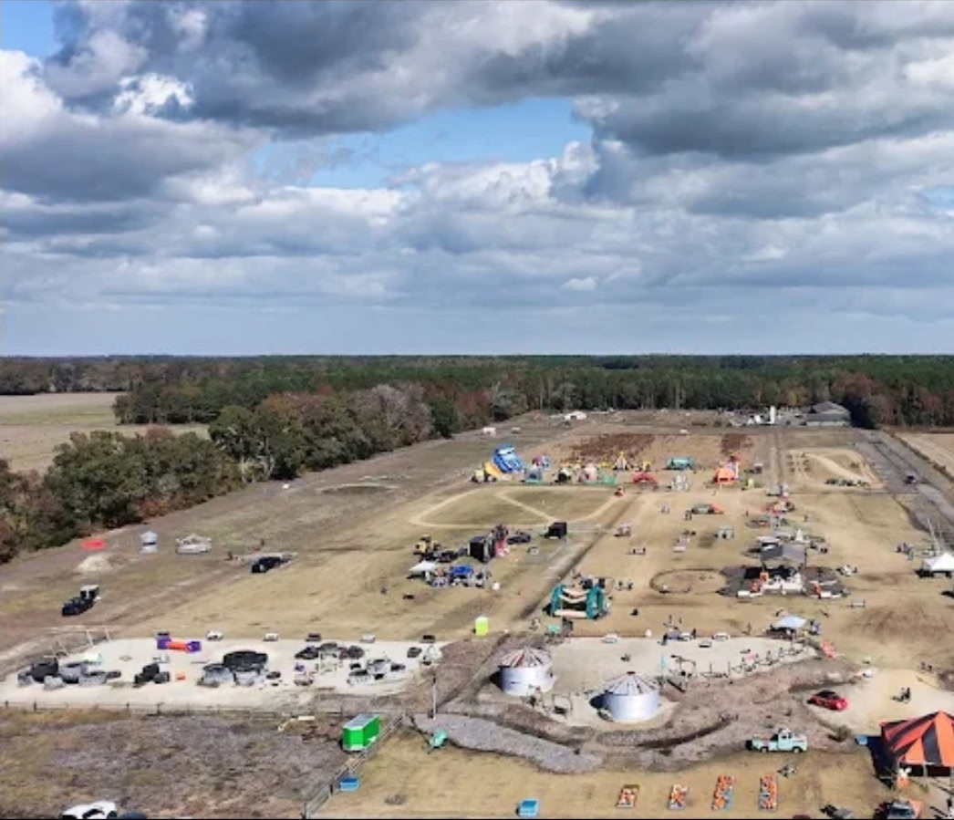 Aerial view of Chubby's Farm grounds with rides, vendor tents, sand area, silos, and parking