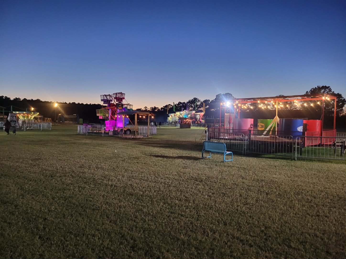 Mini Ferris wheel and string-lit games tent across the field at twilight
