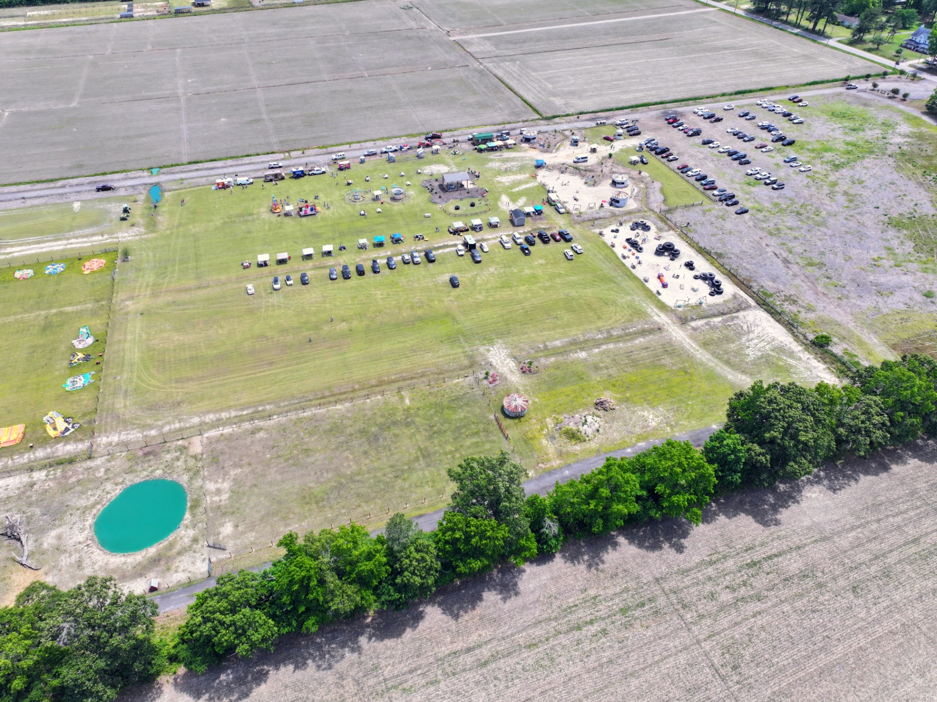 Wider aerial view of Chubby's Farm showing open fields, pond, tree line, and parking area