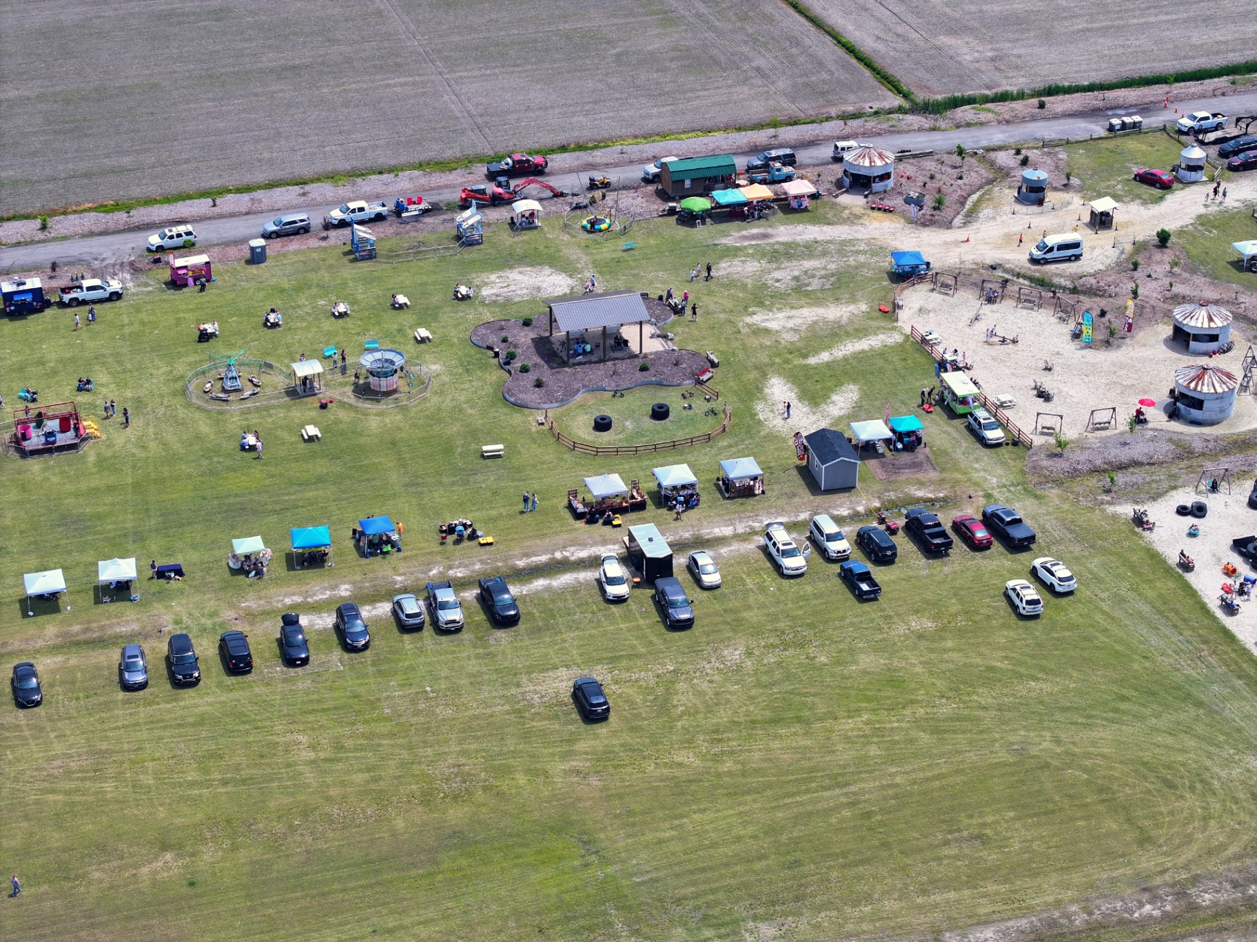 Close-up aerial of Chubby's Farm midway with carnival rides, vendor tents, picnic shelter, and event parking rows